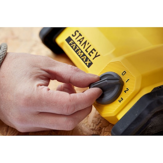 Photo of a hand adjusting the dial on a yellow STANLEY FATMAX SFMCE001B power tool, close-up view.