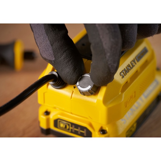 Close-up of a gloved hand adjusting a knob on a yellow STANLEY SFMCE030B tool, front angle view.