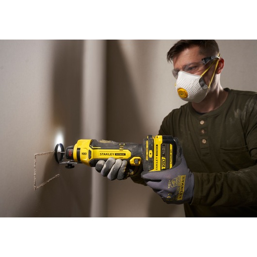 STANLEY SFMCE200B oscillating multi-tool cutting drywall, close-up side angle view.