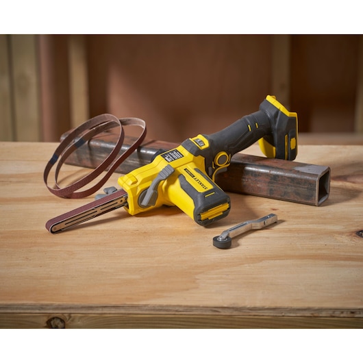 STANLEY SFMCE210B cordless belt file tool, yellow and black, shown on wooden surface with accessories.