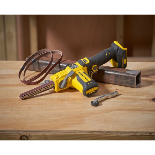STANLEY SFMCE210D2 cordless belt file with sanding belt and wrench on wood surface, front angle.