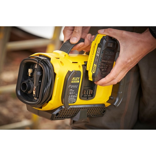 STANLEY SFMCE520B portable yellow air compressor with V20 battery held by a person, outdoor setting.