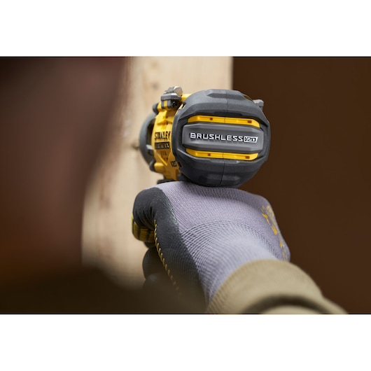 Stanley SFMCF830B brushless V20 impact driver held by gloved hand, close-up side view.