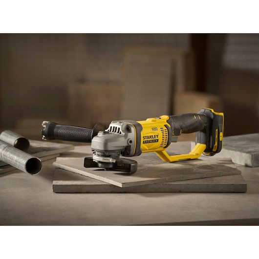 STANLEY SFMCG300B angle grinder with black and yellow design, shown side view on concrete slabs.