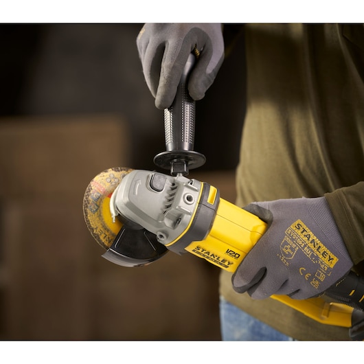 STANLEY SFMCG300B angle grinder held in gloved hands, close-up view of yellow and black tool in use.
