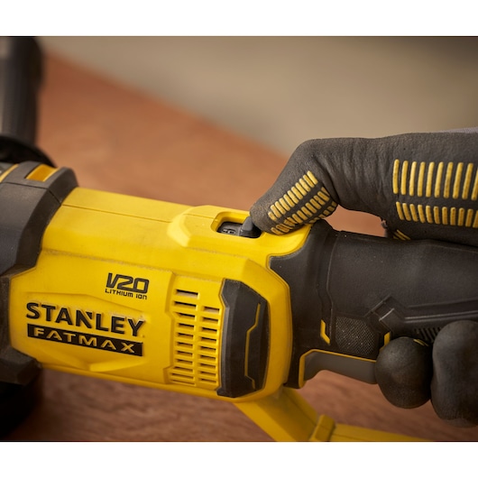 Photo of STANLEY SFMCG300B FATMAX V20 grinder, close-up of power switch with gloved hand.
