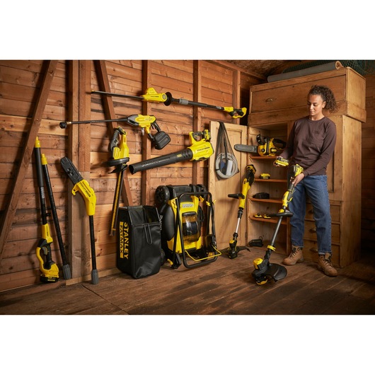 STANLEY SFMCHT855B cordless garden tools and accessories displayed in wooden shed, photo of person holding trimmer.