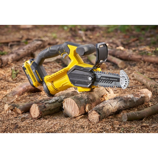 STANLEY SFMCPS415D1 cordless chainsaw photography, yellow and black, shown cutting logs outdoors.