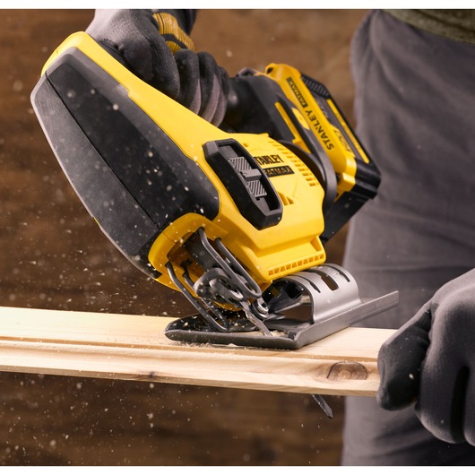 STANLEY SFMCS600B jigsaw cutting wood, close-up view, yellow and black power tool in use.