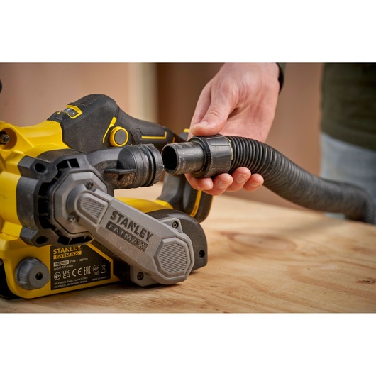 STANLEY SFMCW223B-XJ belt sander with dust hose, close-up angle on wooden surface.