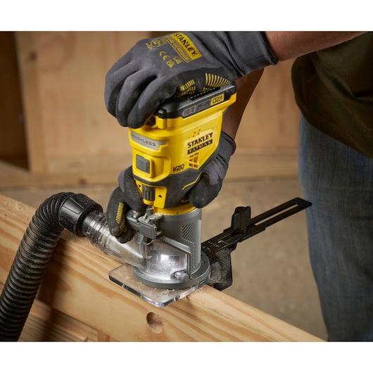 Photo of STANLEY SFMCW400B cordless compact router in use on wood with dust extraction hose attached.