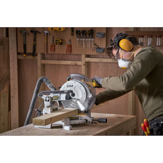 Photo of STANLEY SM1650 miter saw cutting wood in workshop with person wearing safety gear.