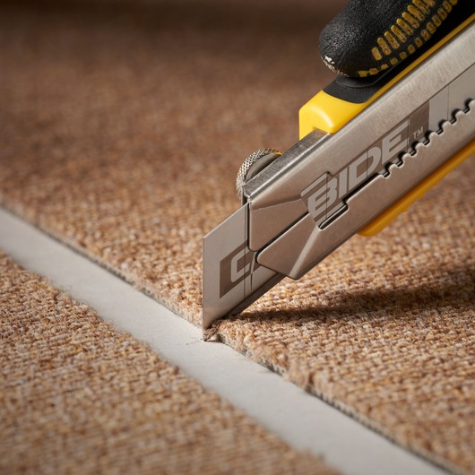 STANLEY STHT0-11825 utility knife cutting brown carpet, close-up showing precise blade edge.