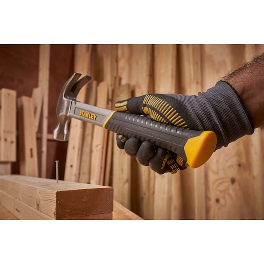 STANLEY STHT0-51309 claw hammer held by gloved hand, near nail and wood, workshop background.