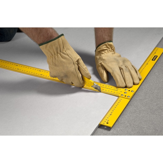 STANLEY STHT1-05894 yellow drywall square used for cutting by gloved hands on a flat surface.