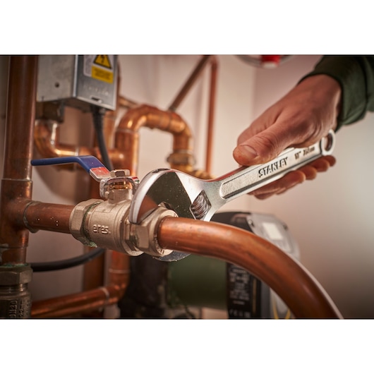 Photo of STANLEY STHT13121-0 adjustable wrench tightening a pipe fitting in a plumbing setup.