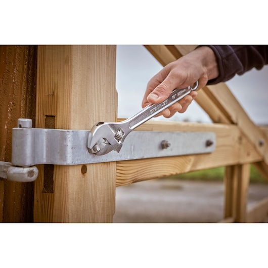 STANLEY STHT13122-0 adjustable wrench tightening a metal bolt on a wooden gate in outdoor setting.