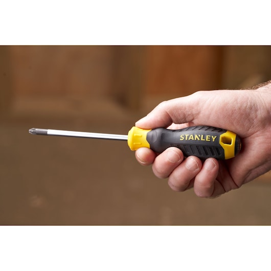 Stanley STHT16163-0 screwdriver with yellow and black handle held in hand, side view, photography.