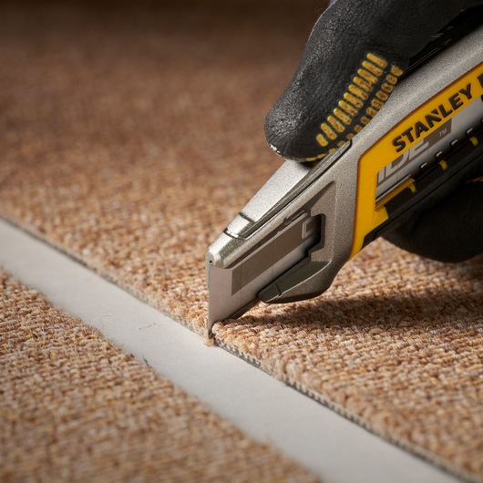 STANLEY STHT2-11818 utility knife cutting carpet, close-up side angle.