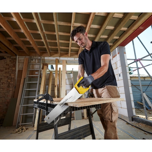STANLEY STHT20348-1 hand saw with yellow handle cutting wood plank on construction site.