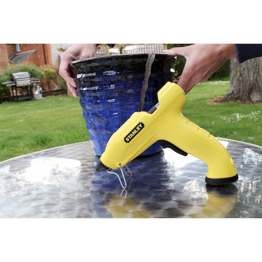 STANLEY STHT6-70416 yellow glue gun on table, used for repairing blue ceramic pot outdoors.