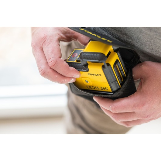 STANLEY STHT77504-1 yellow CROSS 360° laser level being placed into a black carrying pouch by hand.
