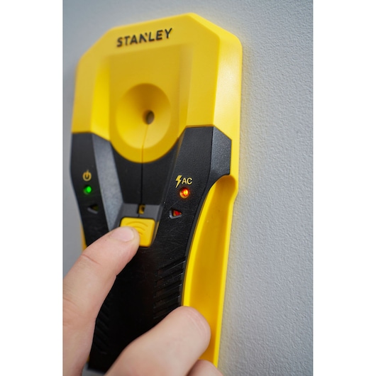 Photo of STANLEY STHT77588-0 digital stud finder against wall, yellow and black hand-held device with indicator lights.