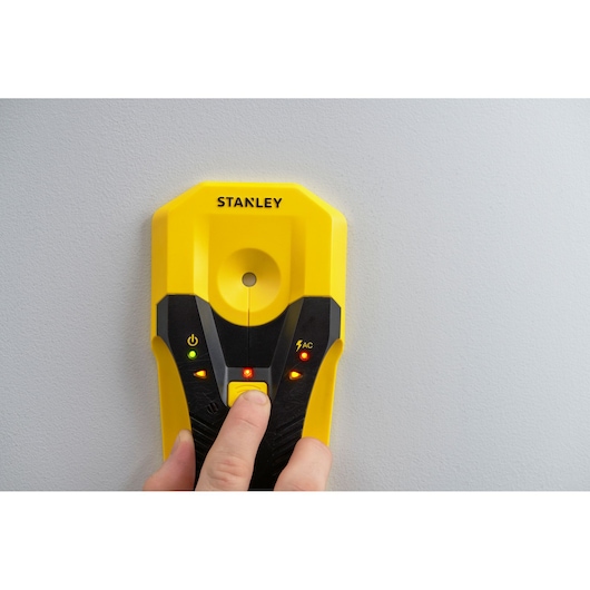 STANLEY STHT77588-0 yellow stud finder held against wall, LEDs illuminated, close-up front angle.
