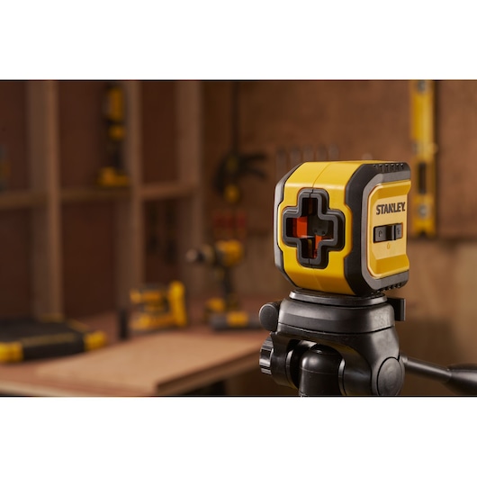 STANLEY STHT77611-0 yellow cross line laser level on tripod in workshop setting.