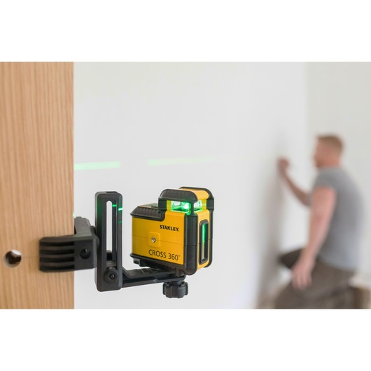 STANLEY STHT77641-1 CROSS 360° laser level mounted on wood, projecting green lines in a workspace.