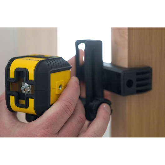 STANLEY STHT77648-1 yellow and black laser level held by hand and mounted on a wooden surface.