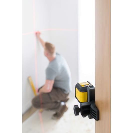 Photo of STANLEY STHT77648-1 laser level on clamp projecting red horizontal and vertical lines in a room.