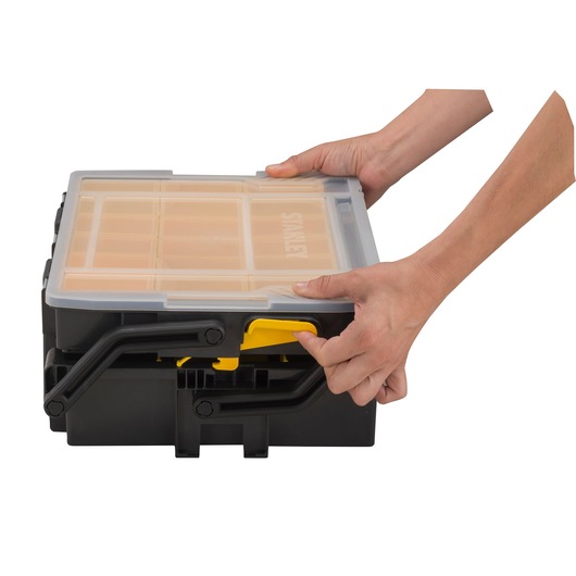 STANLEY STST1-75540 organizer box with transparent lid, black and yellow, hands opening front latch, front angle.