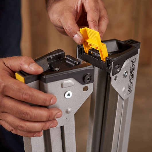 Photo of hands assembling STANLEY STST81337-1 sawhorse leg with yellow locking mechanism.