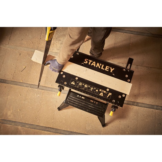STANLEY STST83400-1 workbench holding wood, with gloved hand sawing, top view, workshop setting.
