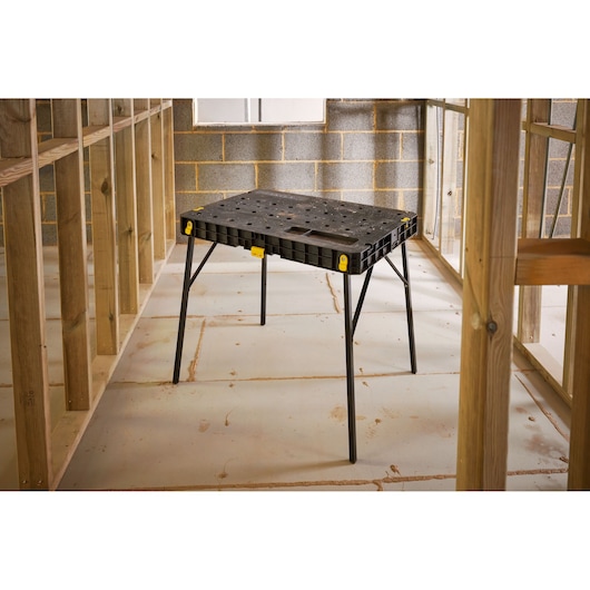 STANLEY STST83492-1 workbench table, black plastic top with foldable legs, shown in construction setting.
