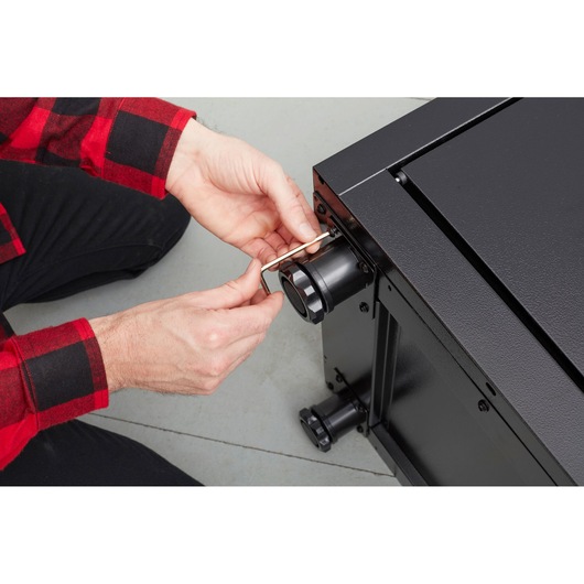 Photo of person using hex key on black STANLEY STST97595-1 tool chest corner, close-up angle.